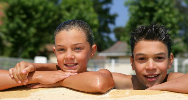 Zwei Kinder am Beckenrand eines Schwimmbads.