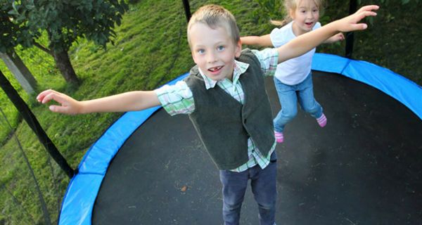 Junge im Vordergrund, Mädchen im Hintergrund hüpfen auf Trampolin und schauen in die Kamera