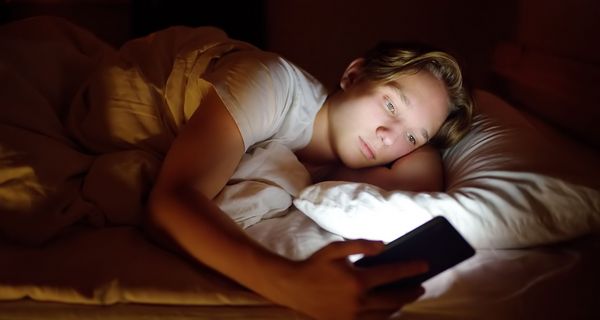 Jugendlicher, liegt im Bett und schaut auf sein Smartphone.