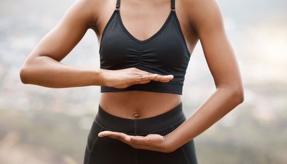 Frau, rahmt mit ihren Händen ihren Bauch ein. 