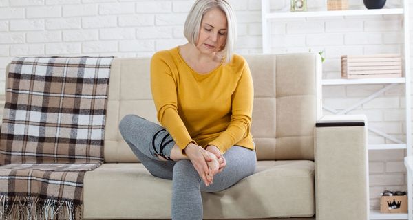 Frau sitzt auf dem Sofa uns hält sich den Fuß.