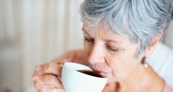 Grauhaarige Frau um die 60 trinkt schwarzen Kaffee aus einer Tasse