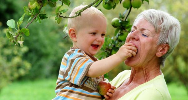 Eine Großmutter beißt in einen Apfel, den ihr ihr Enkel hinhält