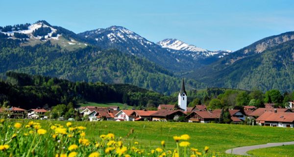 Blick auf ein Dorf im Voralpenland mit Kirchturm und Blumenwiesen