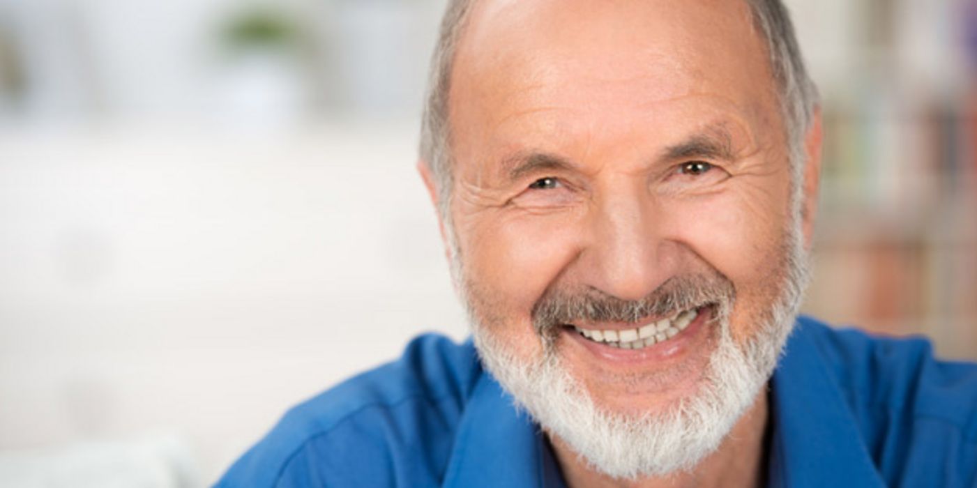 Portraitfoto weißbärtiger, vitaler Mann im blauen Hemd lächelt in die Kamera