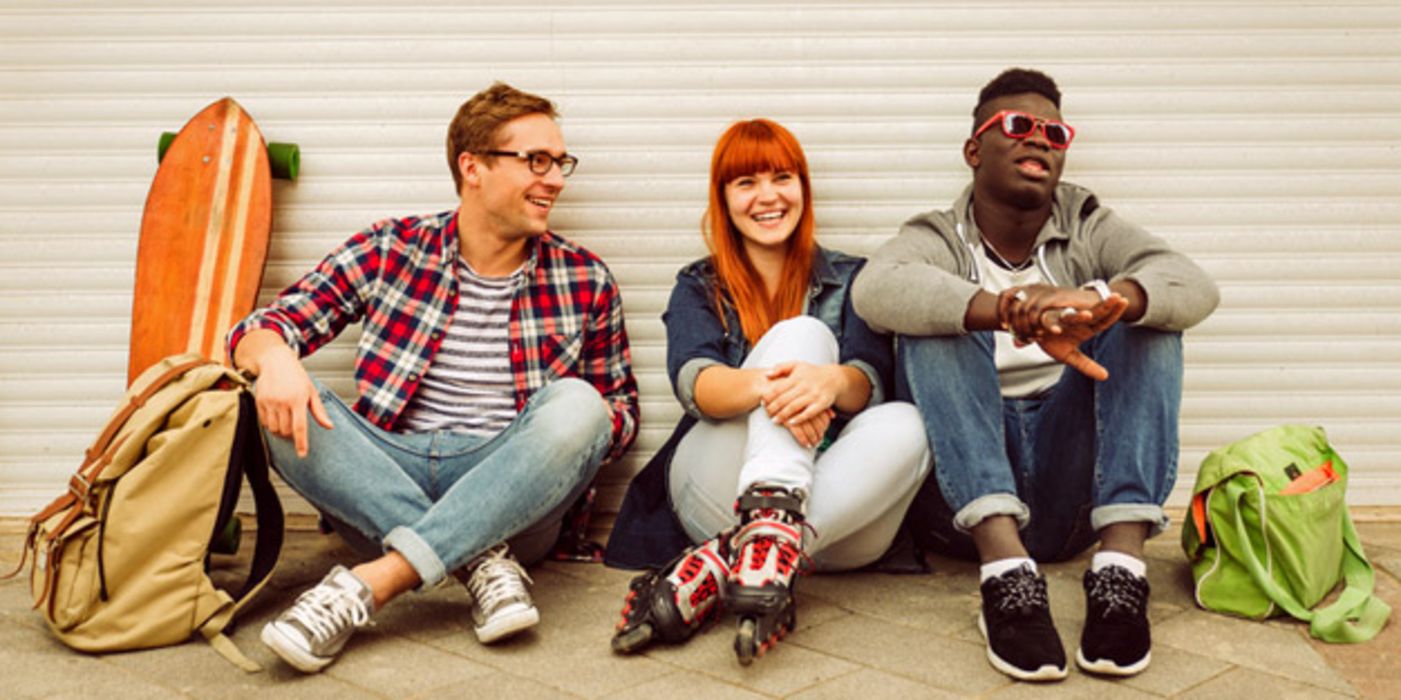 Gruppe von drei jungen Leuten sitzt an einer Mauer und amüsiert sich.