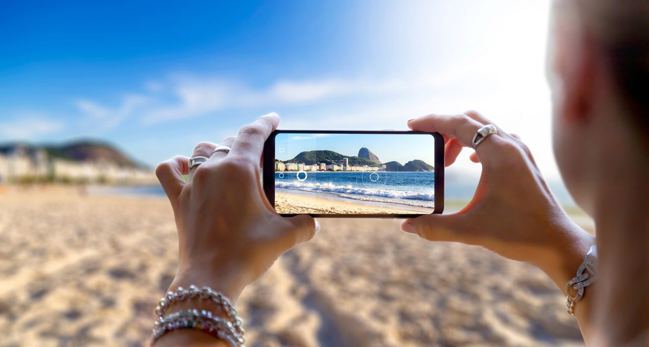 Eine Frau nimmt ein Foto von einem Strand mit einem Smartphone.
