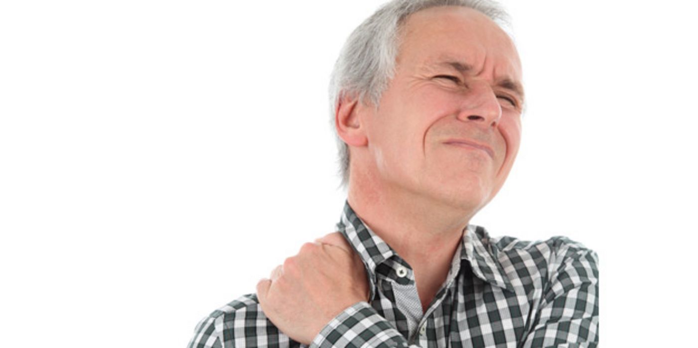 Mittelalter Mann im grau-weiß karierten Hemd greift sich mit schmerzverzerrter Miene an die linke Schulter