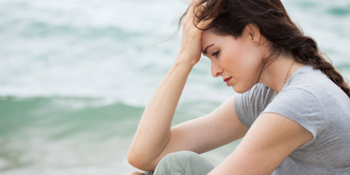 Eine traurige junge braunhaarige Frau sitzt am Strand.