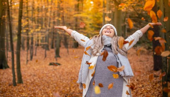 Junge Frau, wirft gut gelaunt Herbstblätter in die Luft.