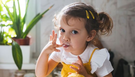 Kleines Mädchen isst Schlagsahne mit den Fingern.