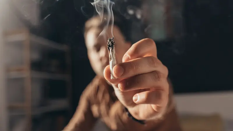 Mann hält einen Joint in die Kamera.