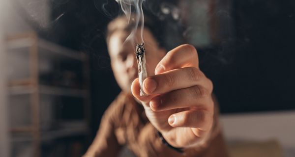 Mann hält einen Joint in die Kamera.
