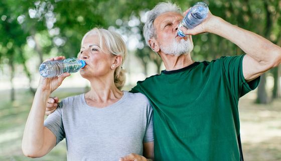 Mann und Frau trinken jeweils Wasser aus Flasche in der Natur/Park