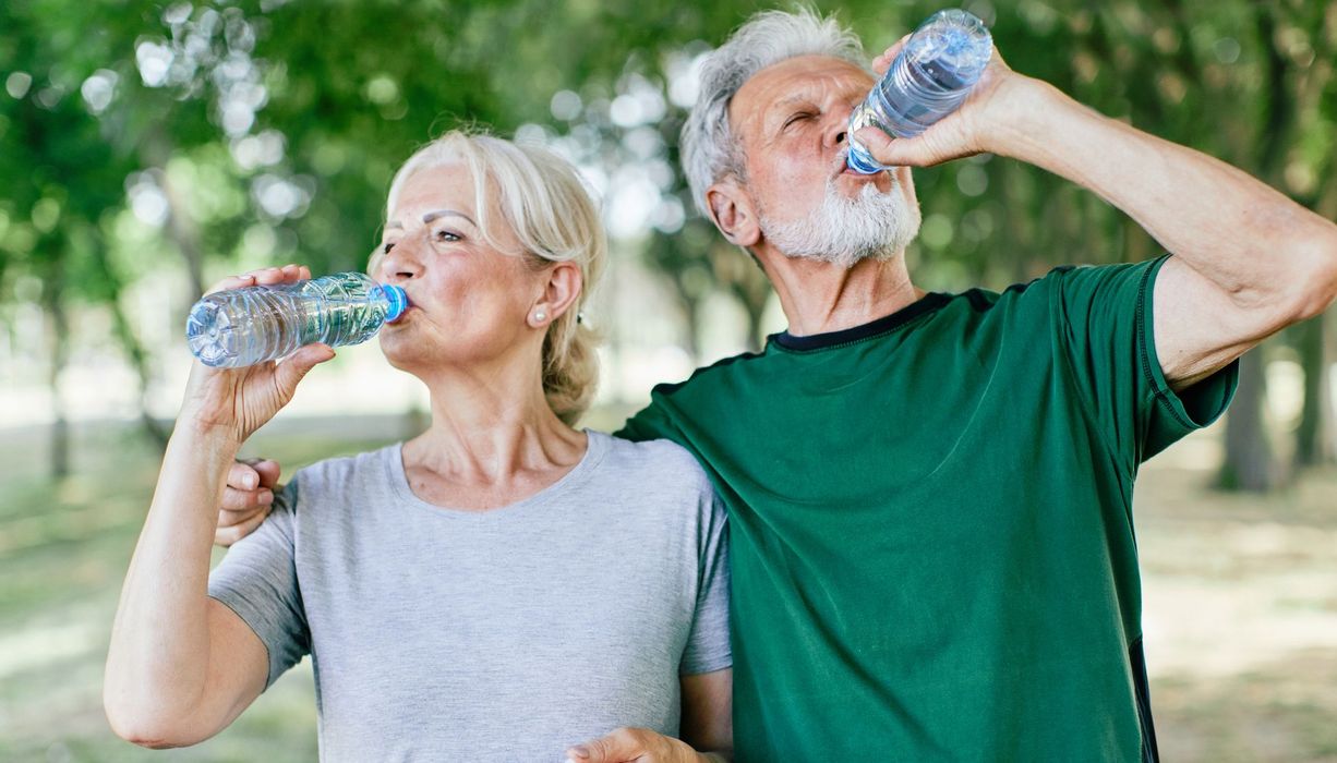 Mann und Frau trinken jeweils Wasser aus Flasche in der Natur/Park
