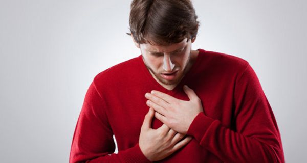 Junger Mann in rotem Pullover greift sich an die schmerzende Speiseröhre