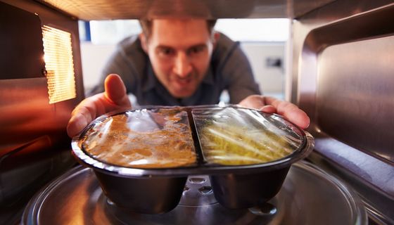 Mann, stellt sich ein Fertiggericht in die Mikrowelle.