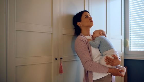 Frau, lehnt sich verzweifelt mit Baby im Arm an einen Schrank.