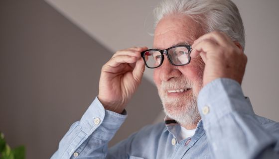 Älterer Herr nimmt lächelnd eine Lesebrille ab.