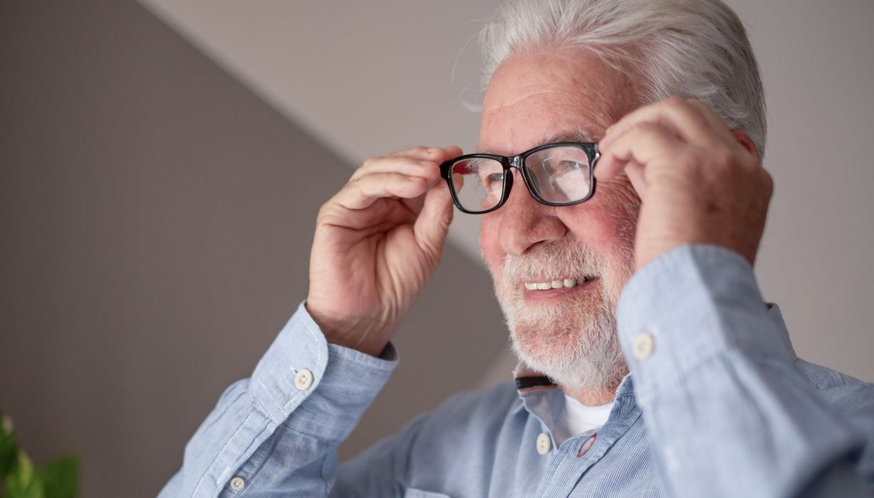 Älterer Herr nimmt lächelnd eine Lesebrille ab.