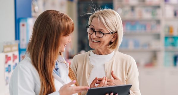 Apothekerin erklärt einer Kundin, etwa 60 Jahre alt, etwas an einem Tablet.