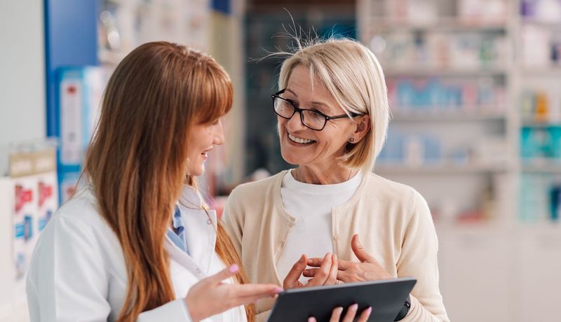 Apothekerin erklärt einer Kundin, etwa 60 Jahre alt, etwas an einem Tablet.