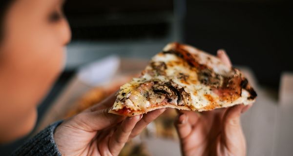 Frau, hält ein Stück Pizza in der Hand.