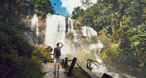 Mann mit Rucksack, steht vor einem großen Wasserfall.