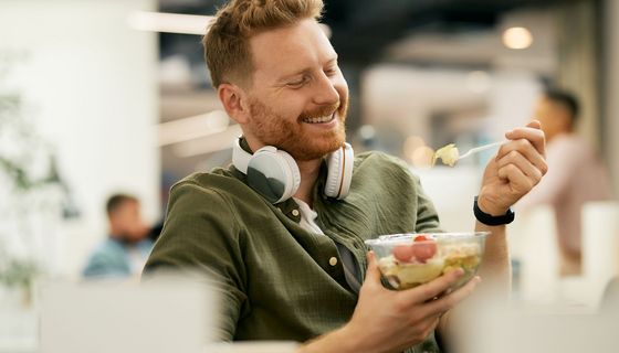 Junger Mann isst Salat in der Mittagspause am Arbeitsplatz.