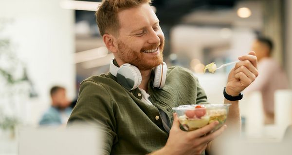 Junger Mann isst Salat in der Mittagspause am Arbeitsplatz.