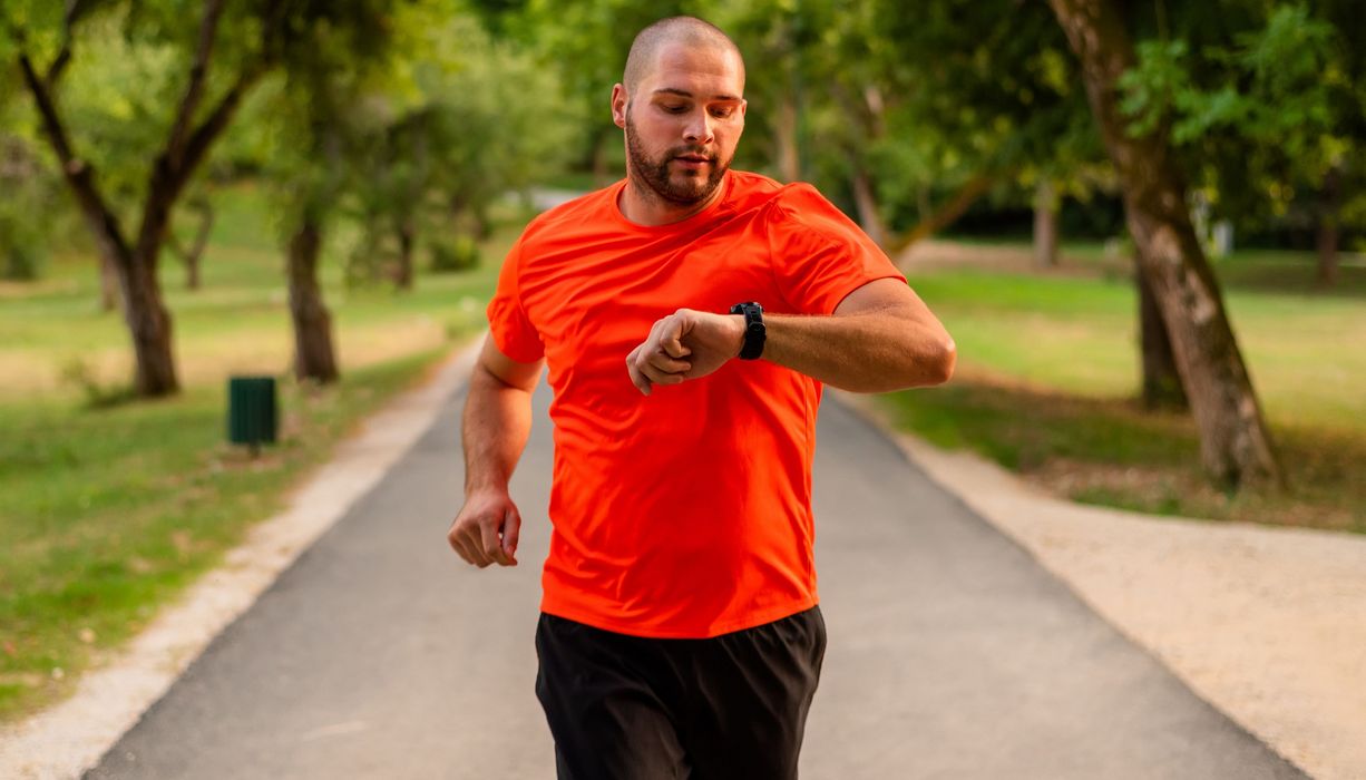 Ein leicht übergewichtiger Mann schaut beim Joggen auf seine Smartwatch.