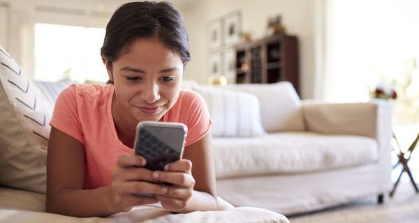 Mädchen, liegt auf der Couch und schaut in ihr Smartphone.