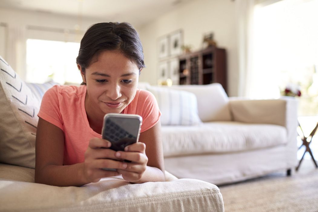 Mädchen, liegt auf der Couch und schaut in ihr Smartphone.