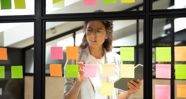 Frau, arbeitet mit bunten Post-its auf einer Fensterscheibe.