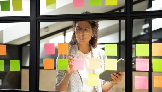 Frau, arbeitet mit bunten Post-its auf einer Fensterscheibe.