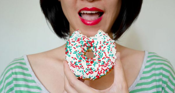 Frau, beißt in einen Donut mit bunten Streuseln.