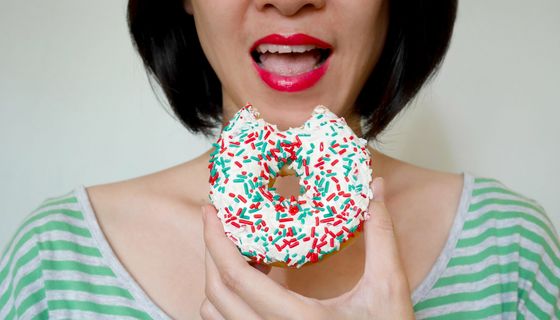 Frau, beißt in einen Donut mit bunten Streuseln.