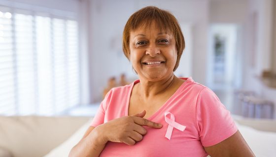 Frau mit rosa T-Shirt und rosafarbener Schleife auf der Brust als Zeichen für Brustkrebs.