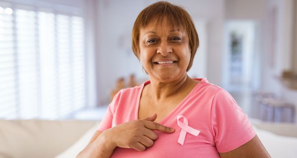 Frau mit rosa T-Shirt und rosafarbener Schleife auf der Brust als Zeichen für Brustkrebs.