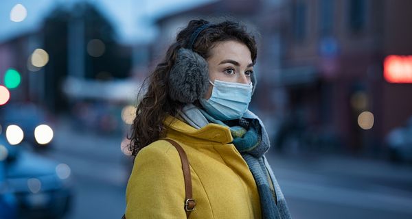 Frau mit Mund-Nasen-Schutz steht draußen in der Kälte