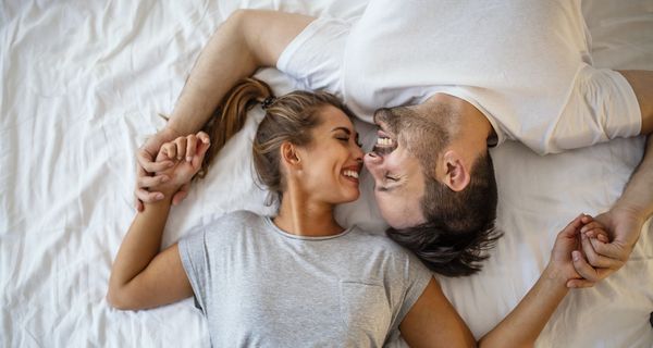 Mann und Frau, liegen zusammen im Bett und lächeln.