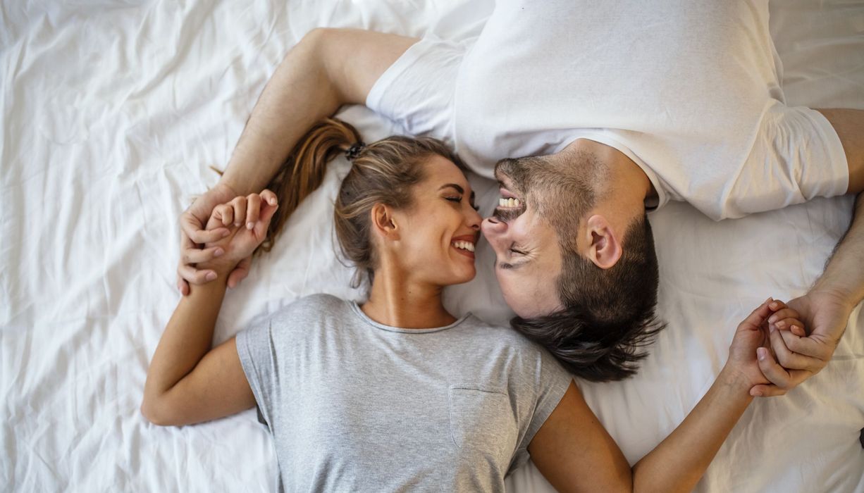 Mann und Frau, liegen zusammen im Bett und lächeln.