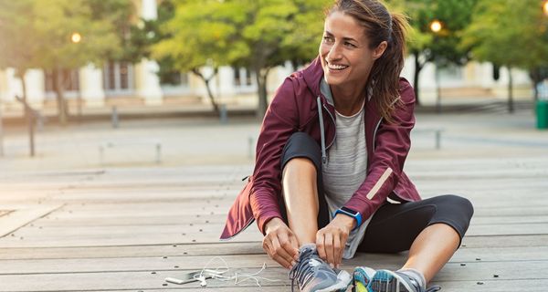 Frau, sitzt draußen und bindet sich ihre Sportschuhe. 