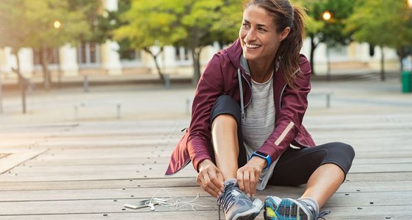 Frau in Sportkleidung sitzt auf Holzplanken.