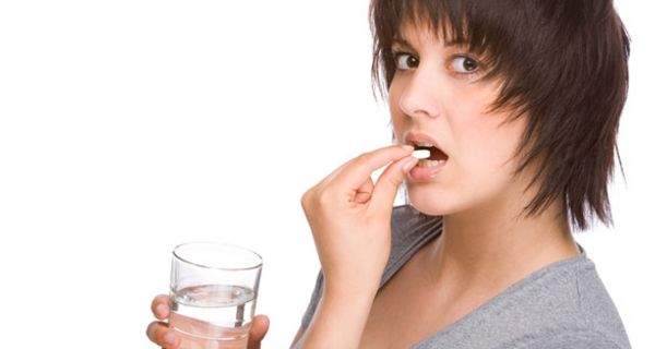 Junge dunkelhaarige Frau bei der Einnahme eines Medikaments, in der Hand ein Wasserglas
