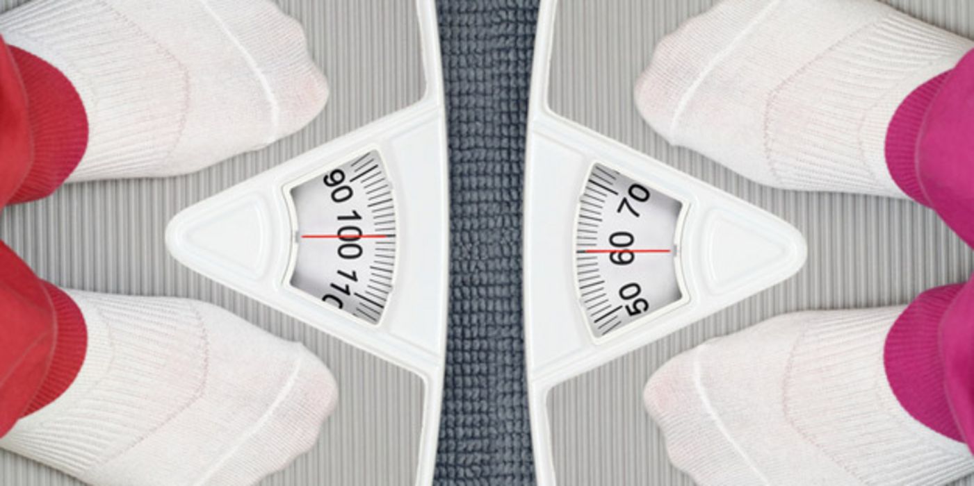 Foto von oben: Füße in weißen Socken auf sich gegenüberstehenden Waagen mit unterschiedlichen Gewichtsanzeigen