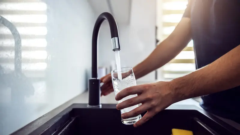 Mann, hält ein Glas unter einen Wasserhahn.