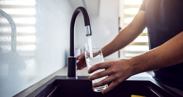 Mann, hält ein Glas unter einen Wasserhahn.