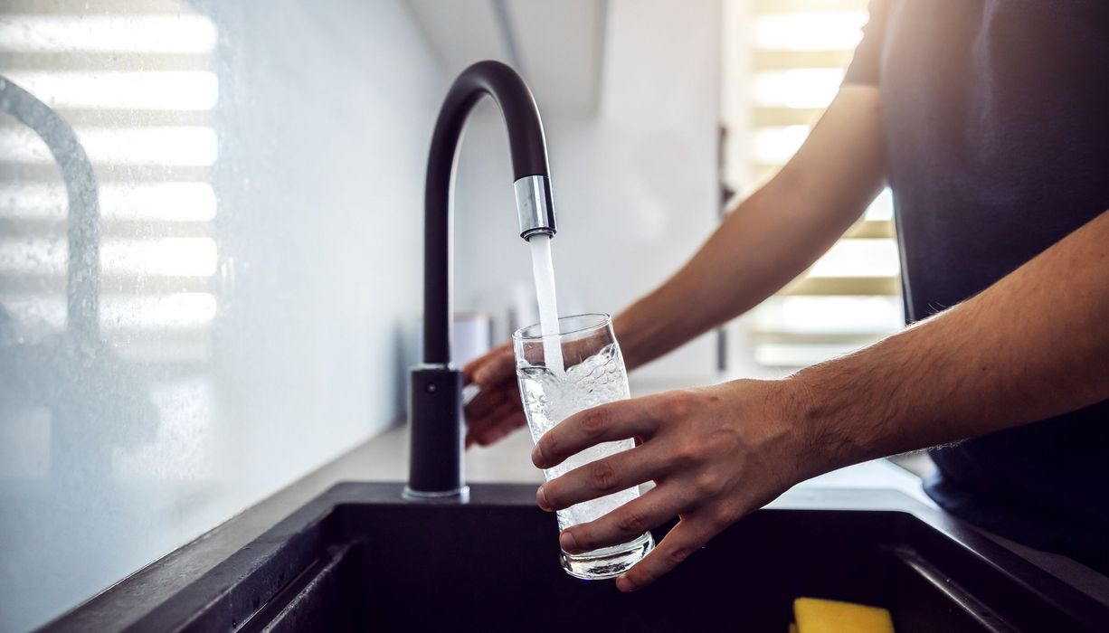 Mann, hält ein Glas unter einen Wasserhahn.