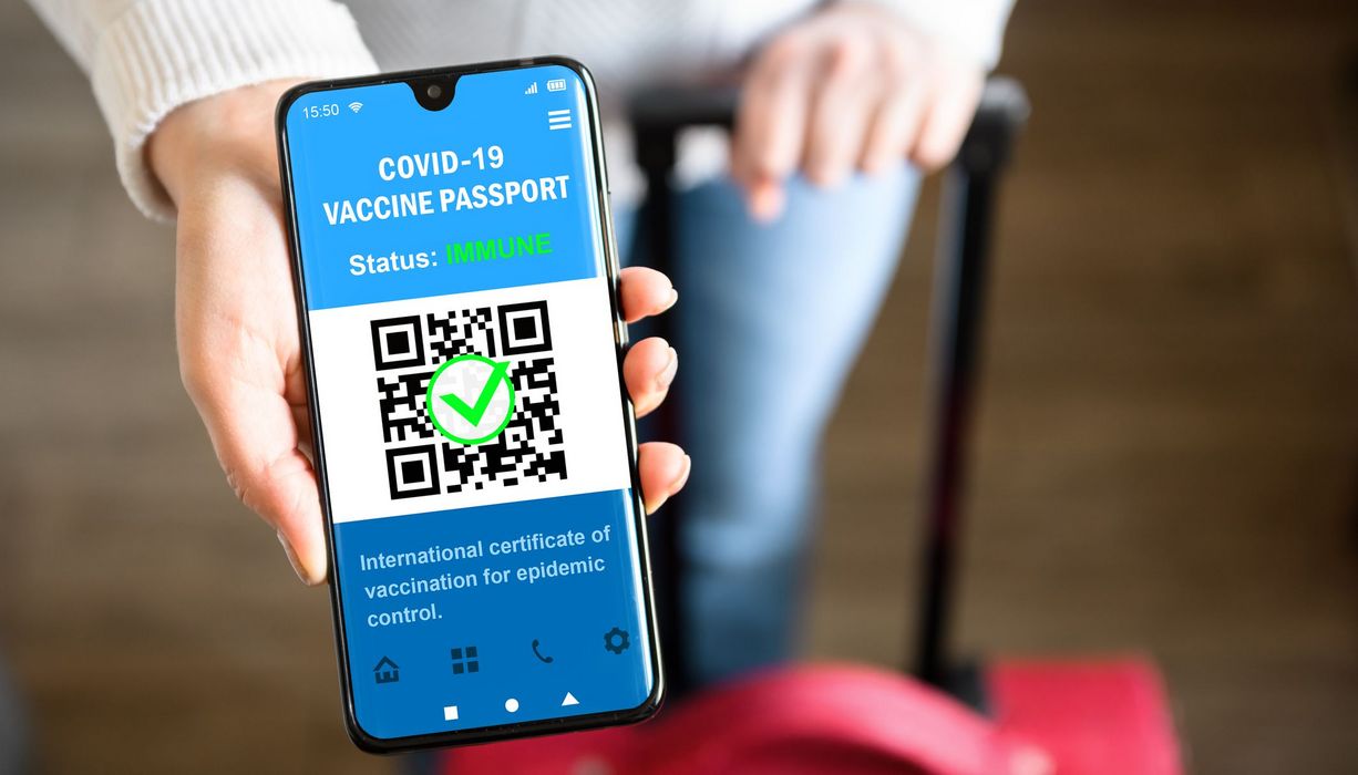 Frau hält ihr Smartphone mit einem digitalen Impfnachweis in die Kamera.
